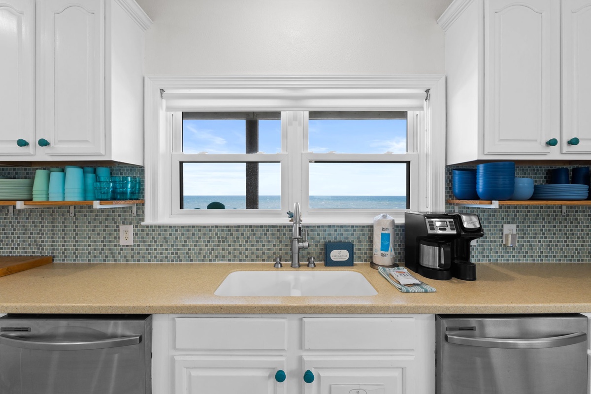 Your kitchen features sleek appliances, beautiful coastal tile backsplash, and a stunning window overlooking the ocean—perfect for morning coffee with a view.
