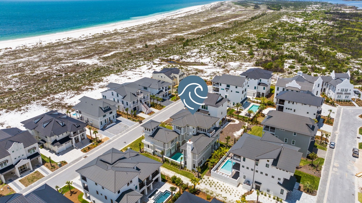 Aerial view of a beachfront community featuring modern homes with pools, nestled between pristine coastline and natural dunes.