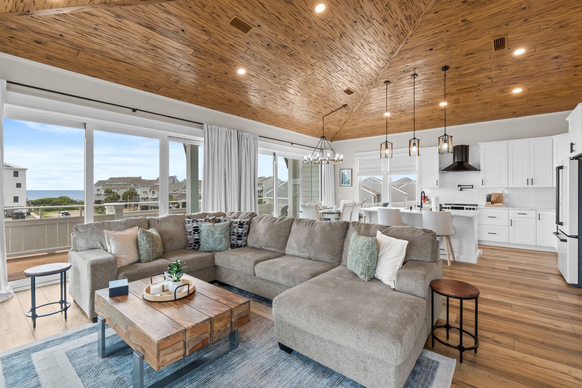 Relax in your open-concept living space with stunning vaulted wood ceilings and coastal views through floor-to-ceiling windows. The modern kitchen and spacious seating invite you to unwind in style.