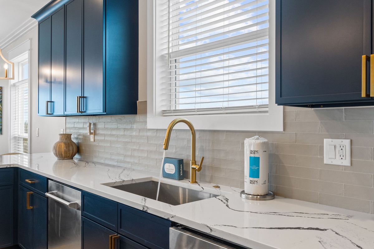 Step into your gourmet kitchen where rich navy cabinetry meets gleaming marble countertops and gold accents. Natural light streams through pristine windows, illuminating a space designed for culinary creativity.
