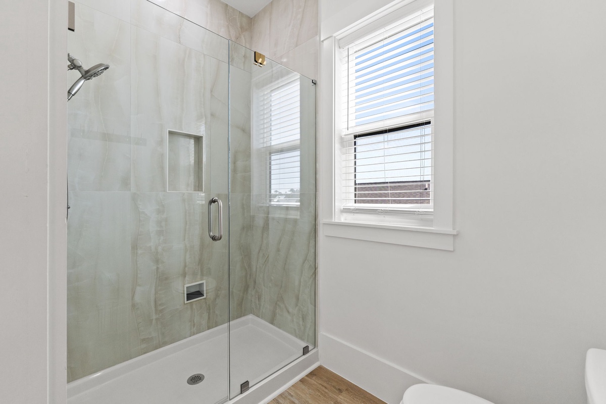 Step into your sleek glass-enclosed shower with elegant marble-look walls and refreshing rainfall showerhead for the perfect morning routine.