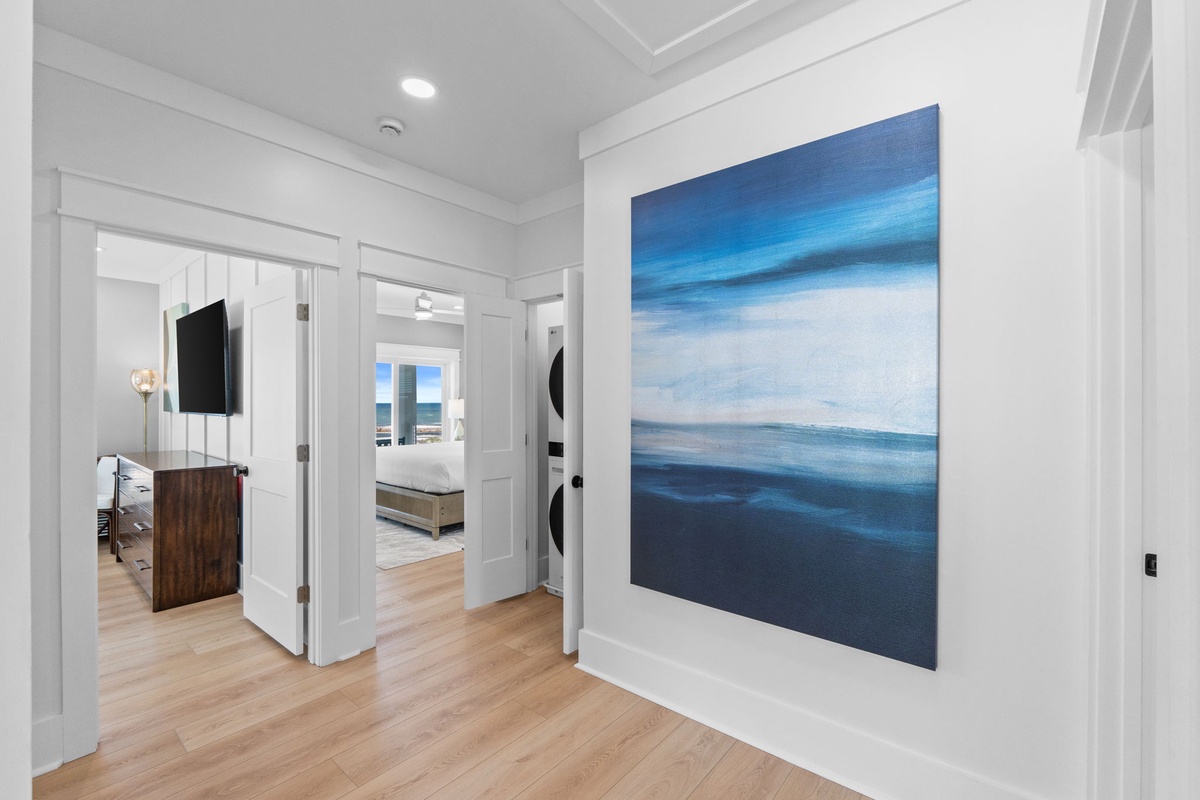 Step into a bright hallway where soothing ocean-inspired artwork sets a tranquil tone. Warm wood floors guide you toward cozy bedrooms, while modern touches like wall-mounted TVs add convenience to your stay.