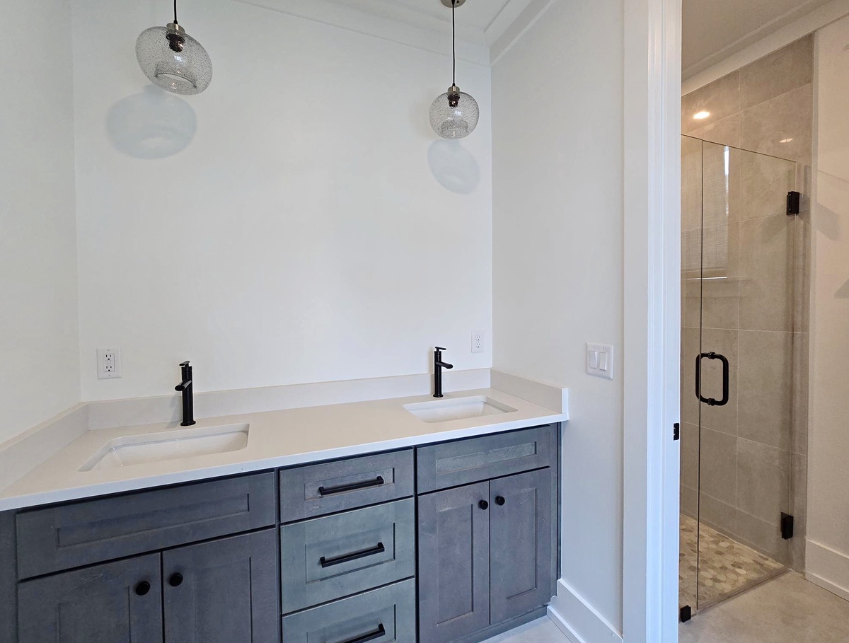 Step into your elegant master bathroom with dual vanities, pendant lighting, and a spacious glass shower waiting for you.
