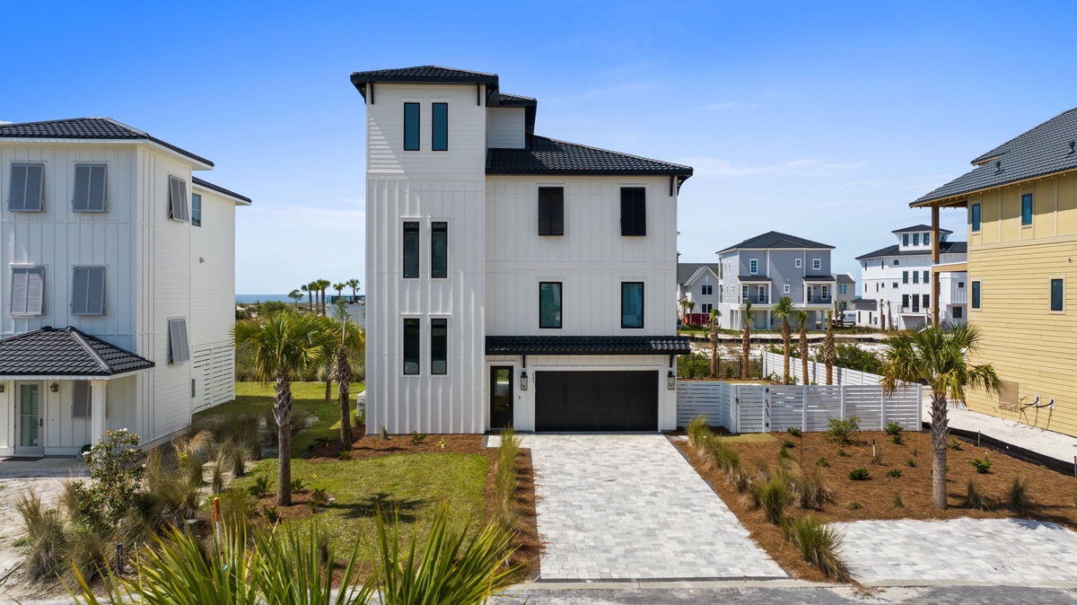 Modern coastal property featuring multi-level architecture with garage parking, situated in a vibrant neighborhood with palm-lined landscaping and convenient paver driveway.