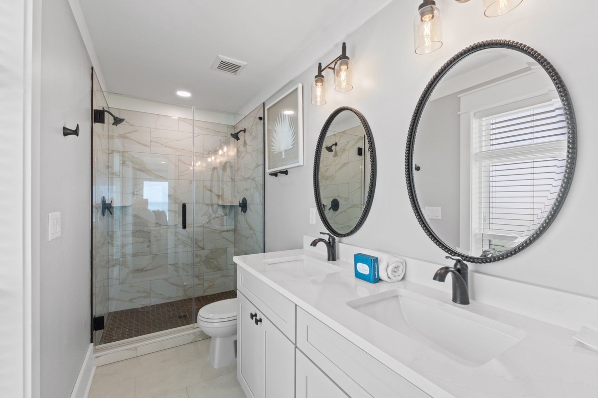 Freshen up in your elegant bathroom with dual vanities, stylish round mirrors, and a spacious glass-enclosed shower with beautiful tile work.