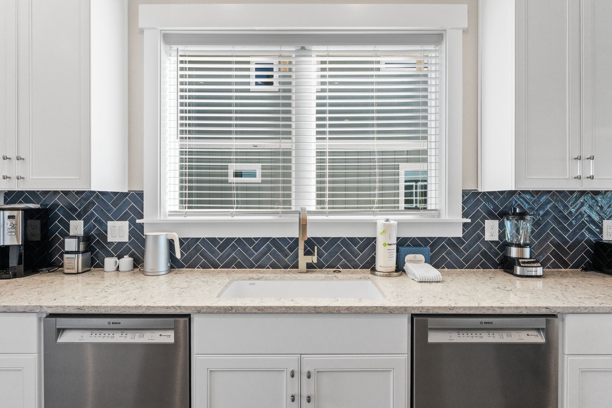 Your modern kitchen features stunning navy herringbone backsplash, dual dishwashers, and pristine countertops perfect for culinary adventures.