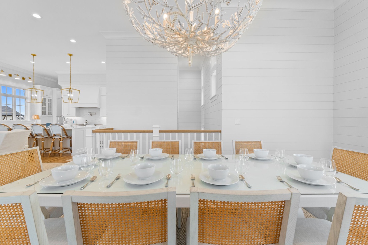 Elegant dining awaits beneath a stunning chandelier, where coastal style meets refined comfort. The spacious table with woven chairs invites memorable meals with loved ones.