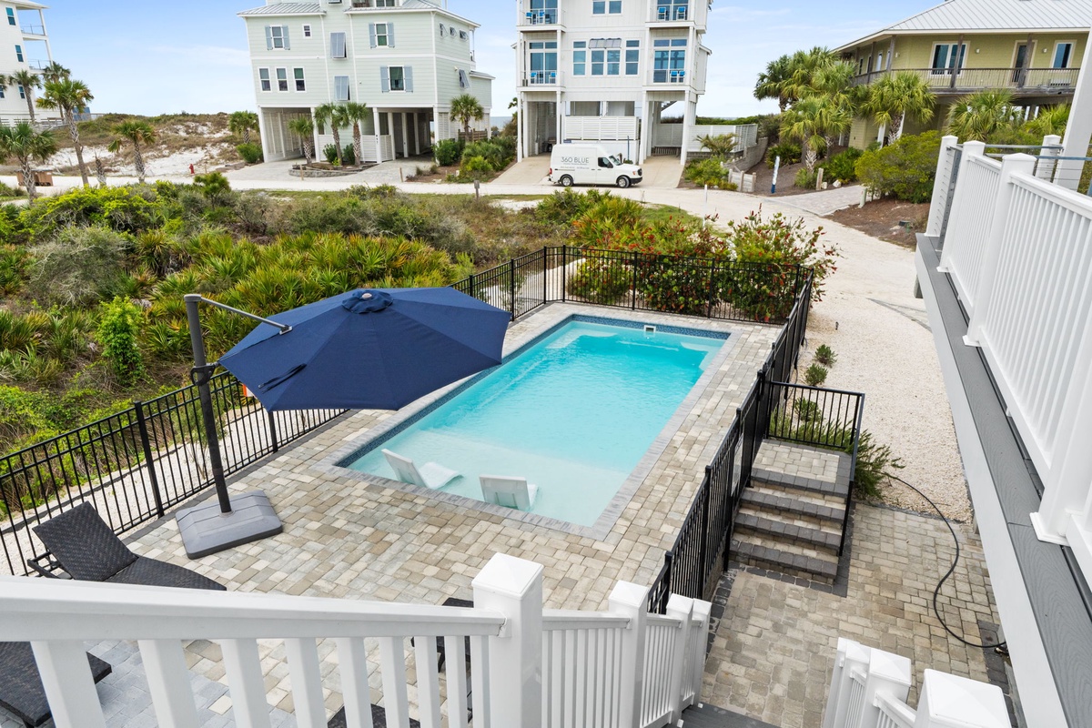 Beach house community with sparkling pool surrounded by lush coastal vegetation and neighboring vacation homes.