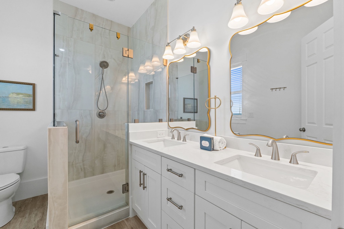 Your spa-like bathroom features a luxurious glass shower, elegant double vanity, and golden accents that create a bright, sophisticated space.