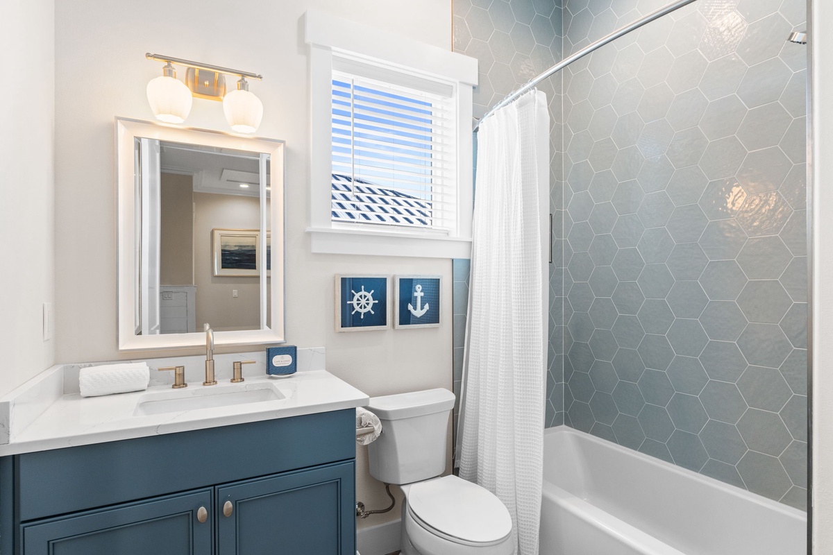 Unwind in your coastal-inspired bathroom featuring beautiful hexagon tile, spacious tub-shower combo, and charming nautical touches that create a refreshing seaside retreat.