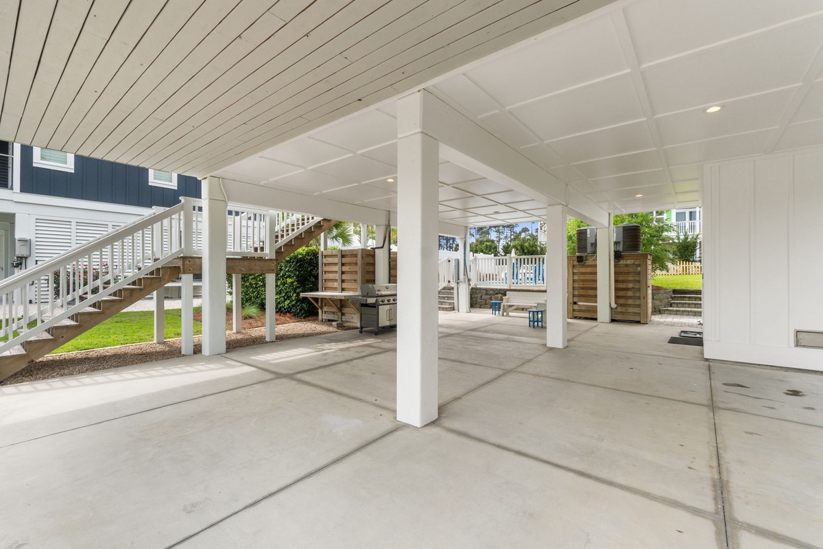 This covered outdoor area provides generous parking and sheltered space, with a BBQ grill and wooden privacy fencing visible throughout the property's ground level.
