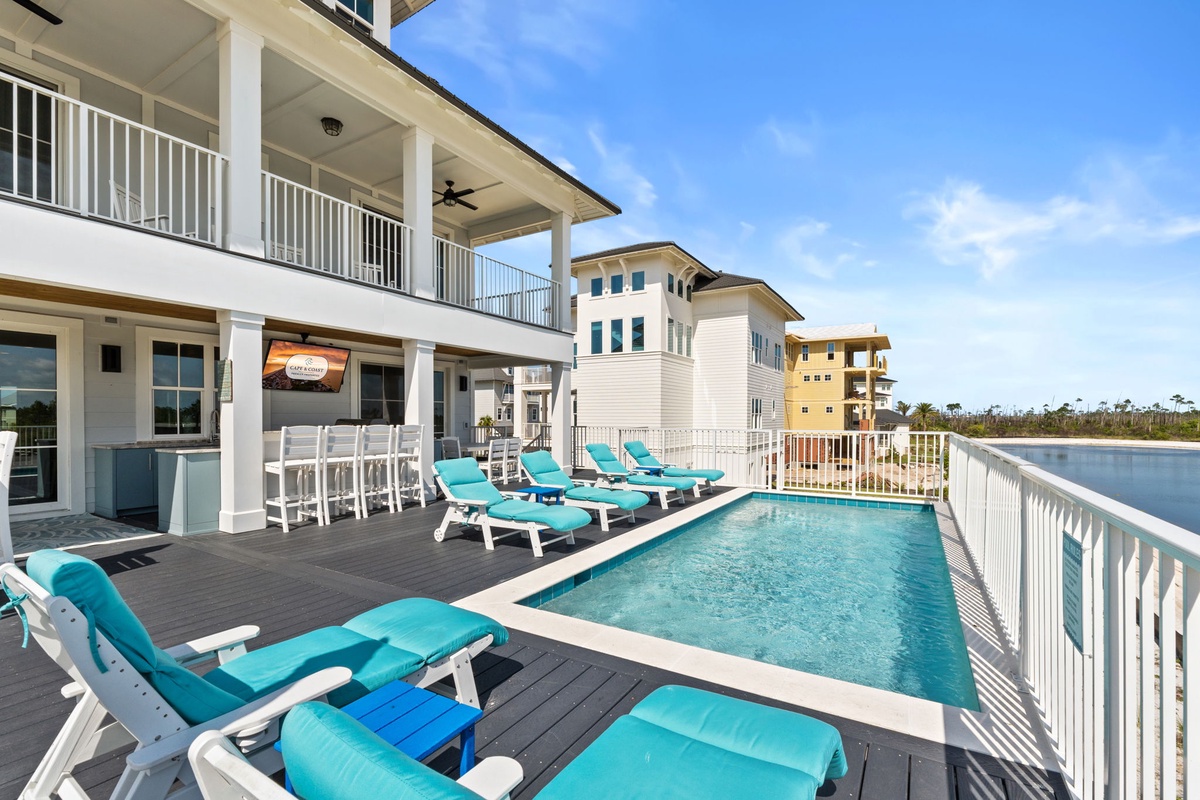 Coastal vacation home featuring a private pool deck with turquoise loungers, covered porch with bar seating, and waterfront access perfect for your beach getaway.