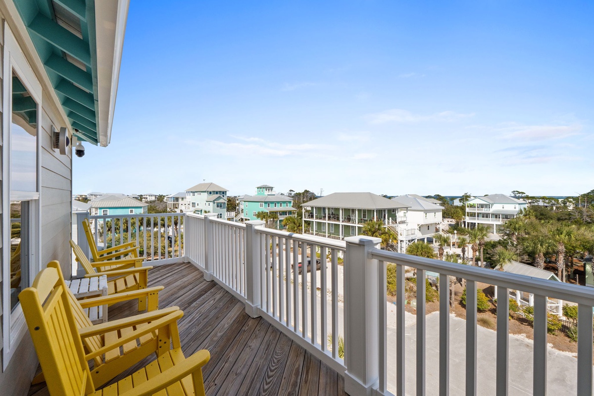 Spacious deck features bright yellow seating overlooking the charming coastal neighborhood below.
