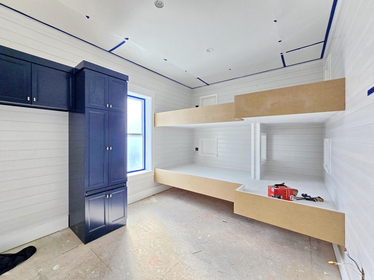 Your sleeping quarters feature modern white shiplap walls with crisp navy trim and built-in bunk beds with warm wood accents, creating a cozy nautical retreat that maximizes space while maintaining clean, contemporary style.