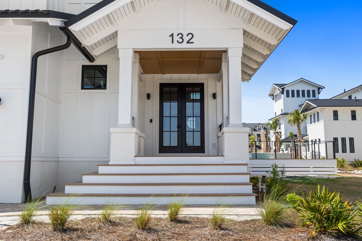 Modern coastal entrance with elegant covered porch and tropical landscaping welcomes guests to this stylish retreat.