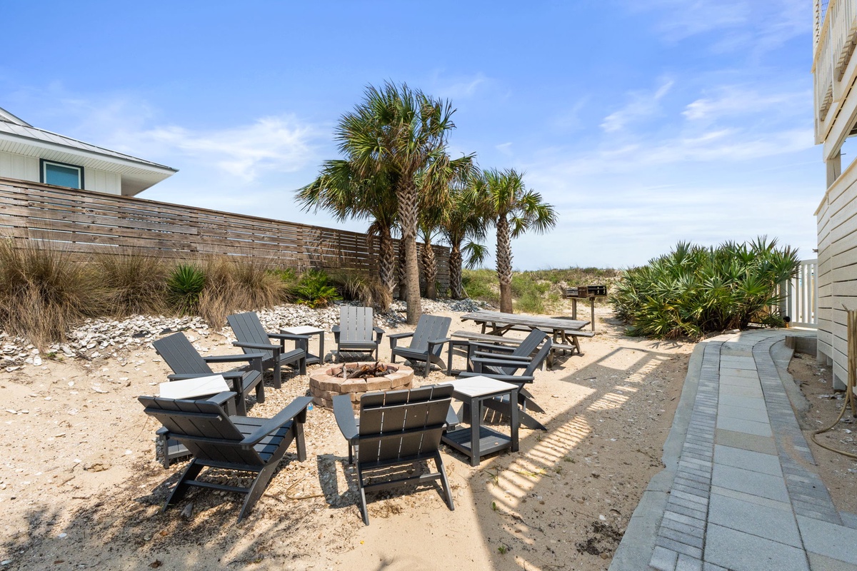 Sandy yard with fire pit, Adirondack chairs, and palm trees—perfect for coastal gatherings and sunset evenings under open skies.