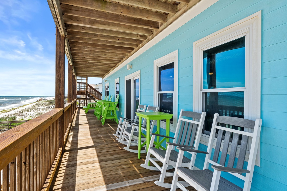 This charming beachfront property features a turquoise exterior with white trim and a welcoming deck equipped with rocking chairs, offering direct views of the sandy shore and rolling waves just steps away.