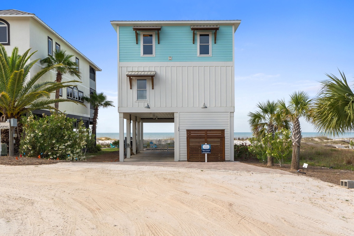 This charming beach house features a bright turquoise and white facade with coastal-inspired design, nestled among palm trees with the sandy shoreline and Gulf waters just steps away.