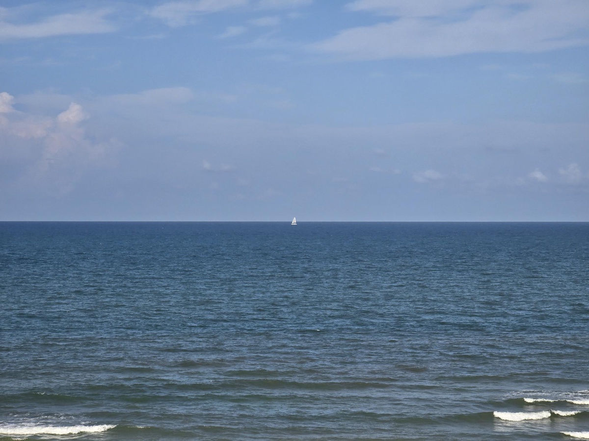 The property enjoys a coastal location with an expansive ocean view, where sailboats dot the horizon and gentle waves lap at the nearby shore.