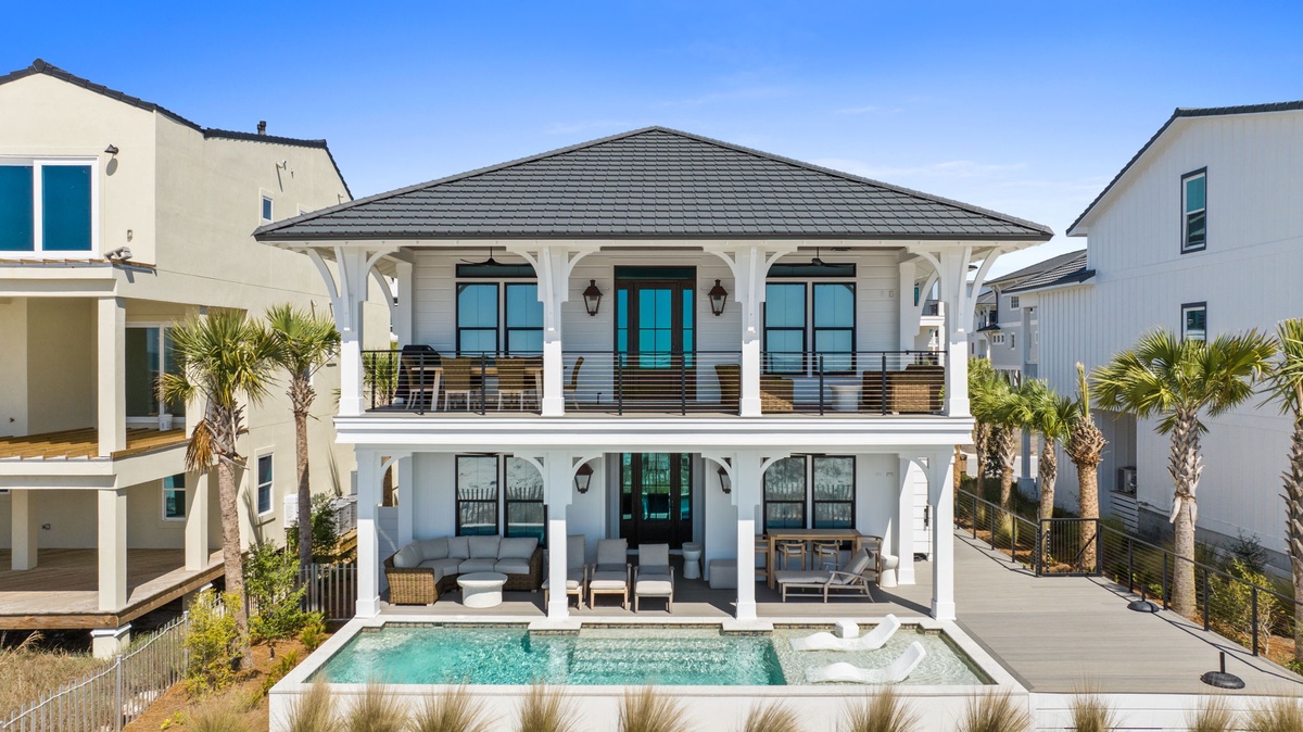 Elegant two-story beach house with covered balconies and private pool amid palm-lined coastal neighborhood.