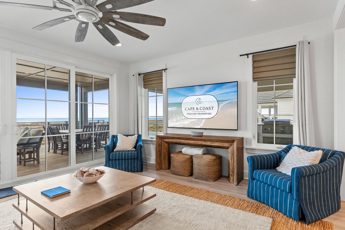 Relax in your coastal haven with sweeping ocean views through expansive windows, plush seating, and gentle breezes from the ceiling fan.