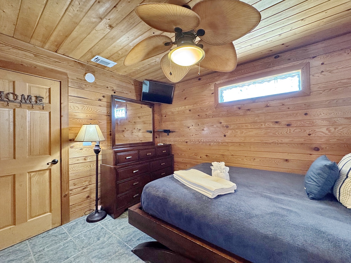 Your cozy cabin bedroom features warm wood walls, comfortable bedding, and thoughtful amenities for a peaceful mountain retreat.