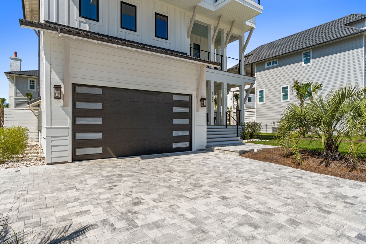 Modern beach house exterior featuring sleek architectural details, covered deck with coastal charm, and convenient driveway parking in a serene neighborhood setting.