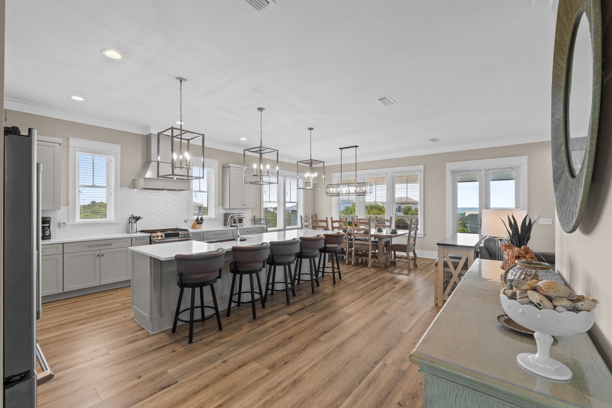 Your open-concept kitchen and dining space flows seamlessly, with modern pendant lights, spacious island seating, and beach views through every window—perfect for gathering and making memories.
