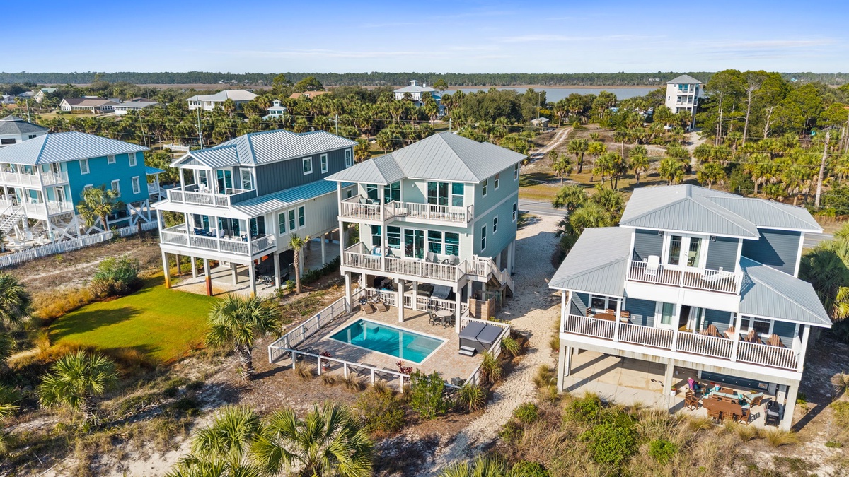 Aerial view of coastal vacation rental homes featuring elevated architecture, private pools, and tropical landscaping in a beach community setting.