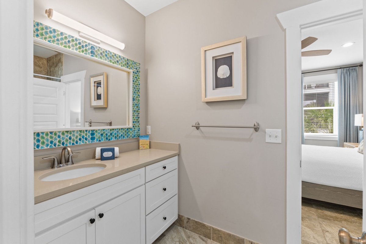 Your private en-suite features a coastal-inspired vanity with calming turquoise mosaic tile accents, plenty of counter space, and soft lighting to start your mornings feeling refreshed and relaxed.