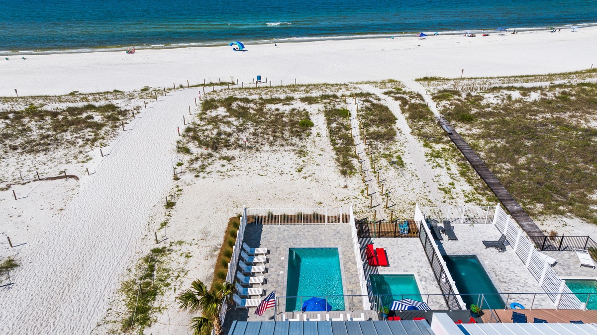Aerial view of beachfront property with pool facilities, situated steps from white sandy shores and Gulf waters.