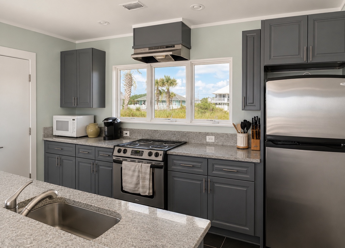 Your spacious kitchen features modern appliances, granite countertops, and large windows framing palm trees and coastal views—perfect for preparing beach-day meals.