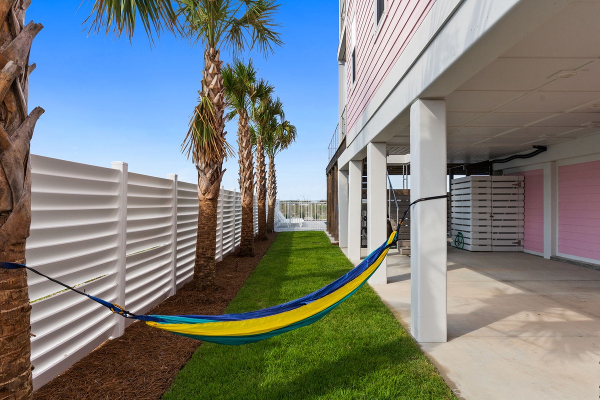 Arrive to swaying palms and a vibrant hammock strung between posts—your perfect spot to unwind in the shade beside fresh green grass.