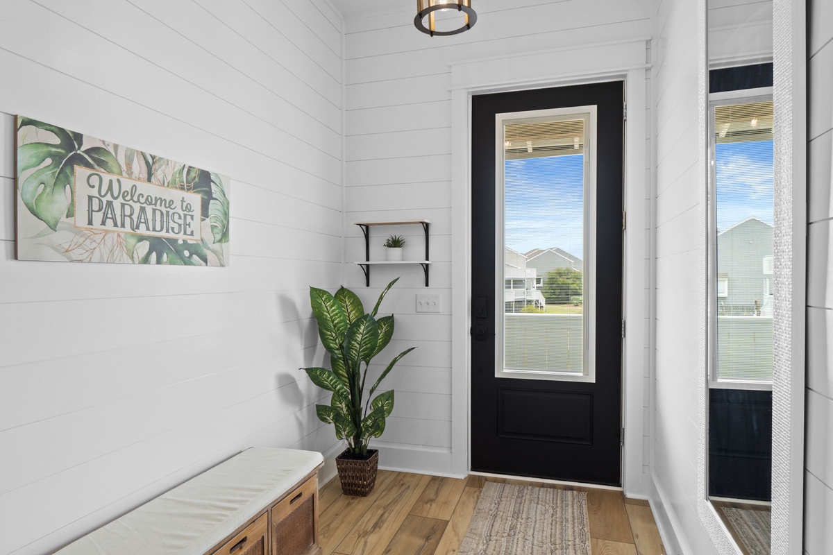 Bright, welcoming entrance with shiplap walls and warm wooden floors greets you with coastal charm. Natural light floods through glass doors, setting a relaxed, beachy mood.