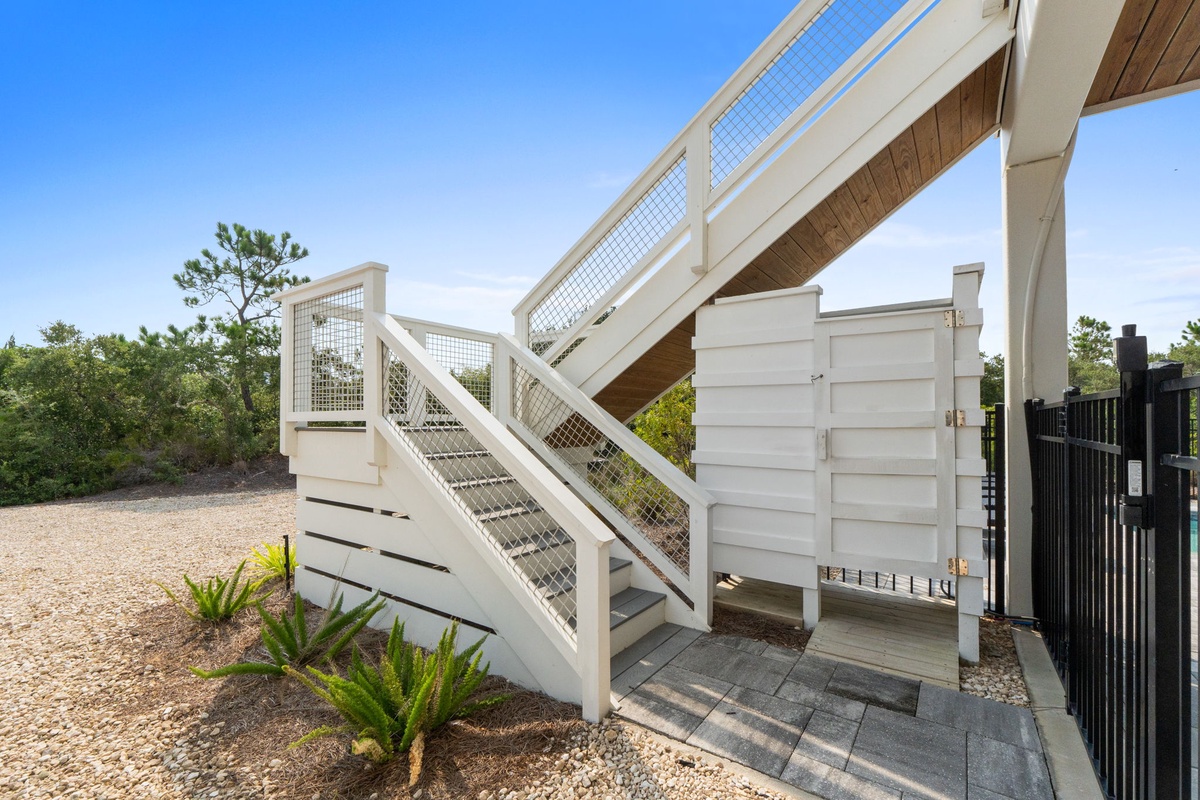 Coastal charm begins at this elevated entrance with clean white railings and natural landscaping, welcoming you to your beachside retreat under open sky.