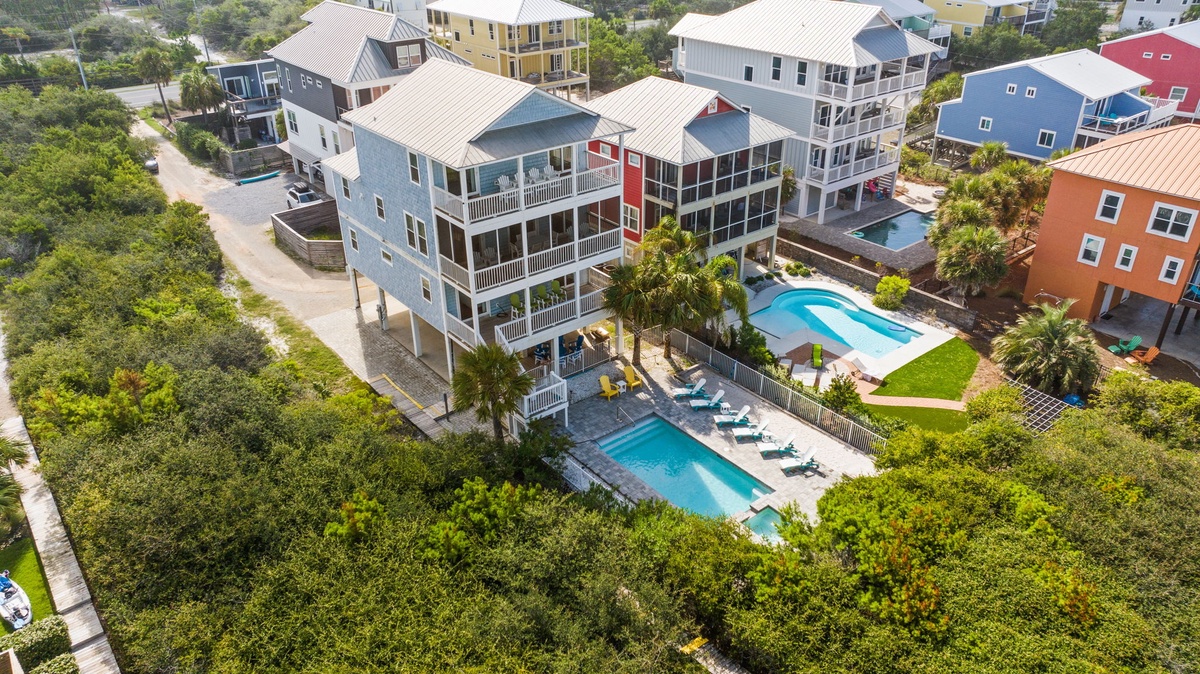 Aerial view of colorful coastal vacation homes in a lush neighborhood setting, featuring private pools and easy beach access.
