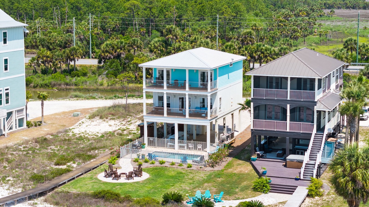 Aerial perspective of two coastal vacation homes surrounded by tropical landscaping, lush greenery, and palm trees in a quiet neighborhood setting.