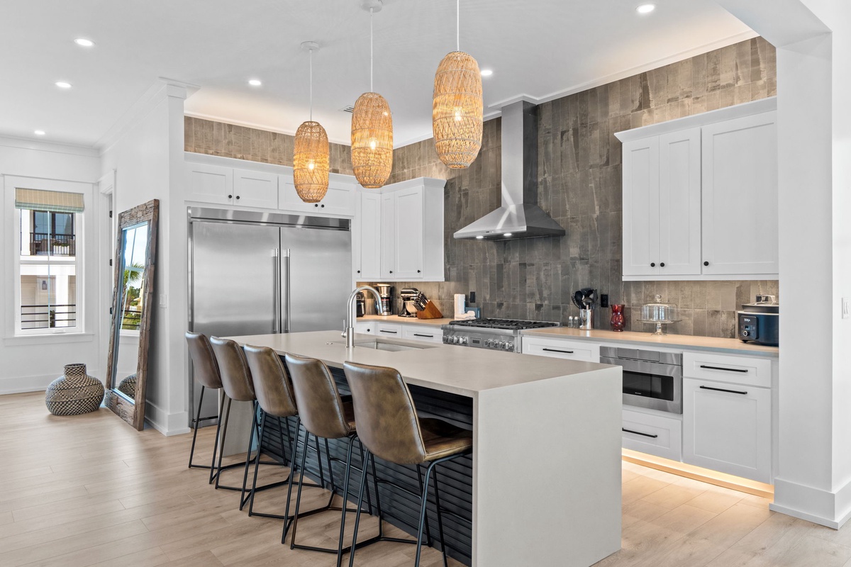 Your gourmet kitchen features a spacious island with seating for four, stainless steel appliances, and coastal-inspired lighting that creates a warm, inviting atmosphere perfect for preparing meals and gathering with loved ones.