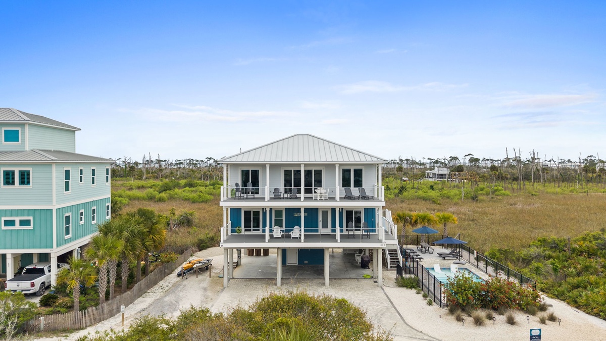 Modern coastal home elevated on stilts with expansive balconies overlooking natural wetlands and neighboring beach houses.