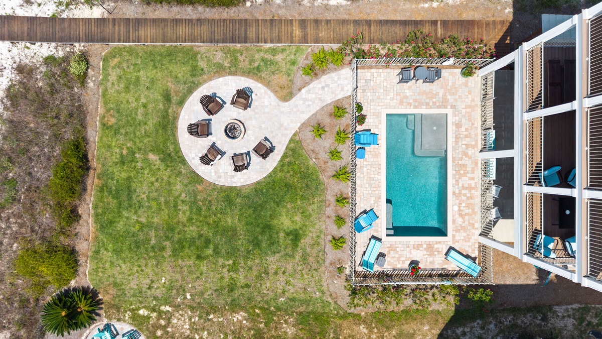 Aerial view of a modern vacation rental featuring a private pool, garden lounging area, and spacious outdoor spaces surrounded by natural landscaping and fencing.