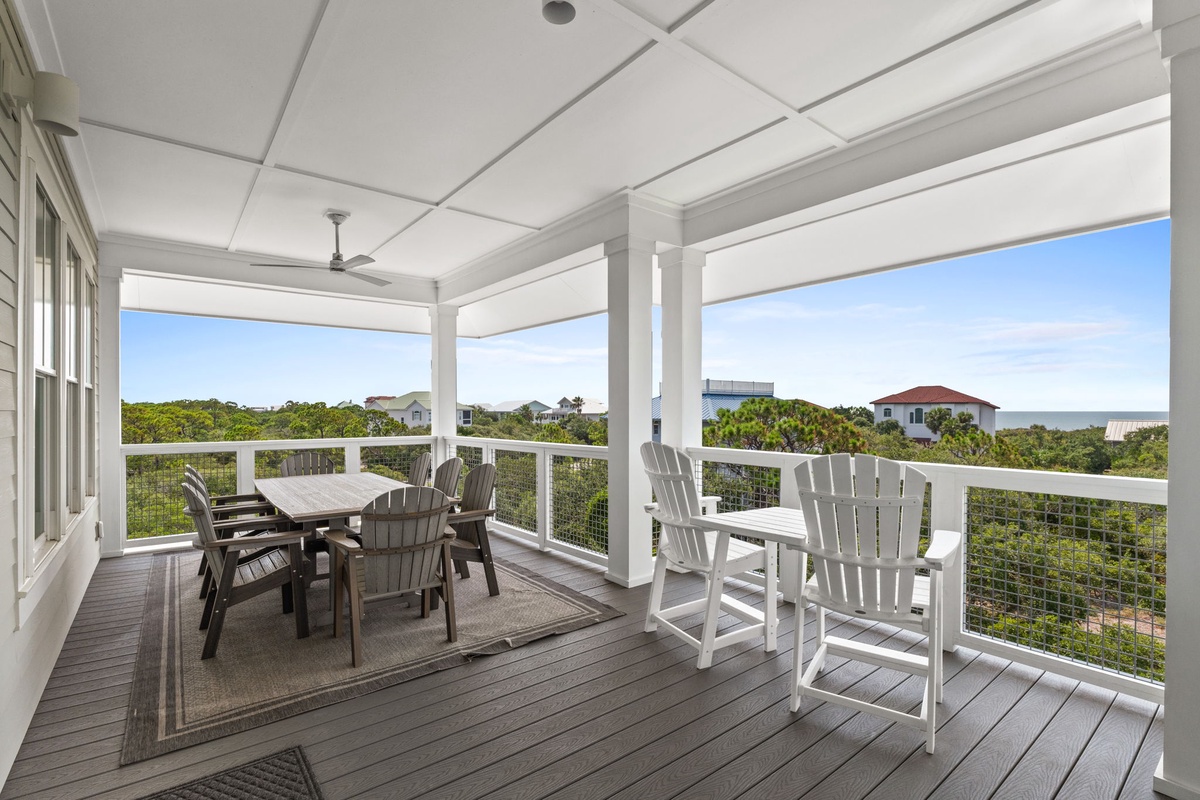 Step onto your private covered porch, where coastal breezes meet classic Adirondack seating and dining space. Beyond the greenery, catch glimpses of the ocean sparkling in the distance.