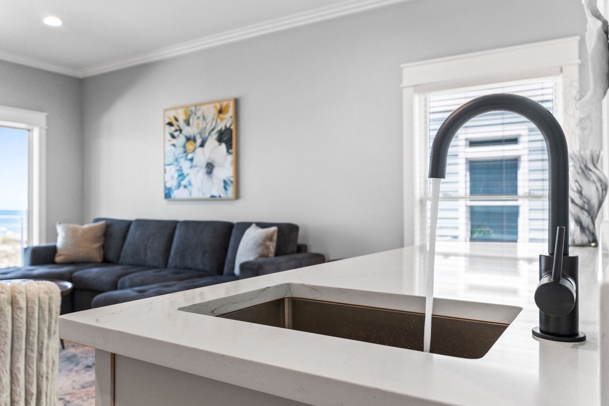 Your open-concept space features a sleek kitchen island that flows into a cozy living area, where a plush sofa invites relaxation and ocean breezes drift through the window.