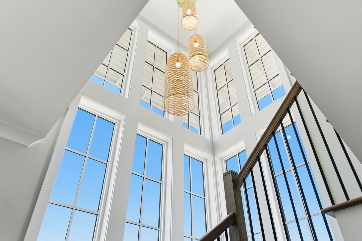 Sunlight streams through soaring windows illuminating a stunning woven pendant fixture, creating a bright, airy welcome as you step inside.