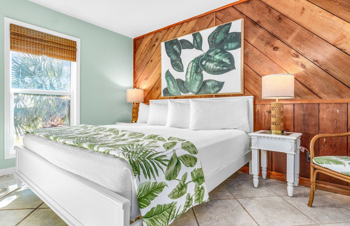 Drift off beneath tropical-themed linens in a king master retreat, where warm wood walls and soft natural light create the perfect peaceful escape.