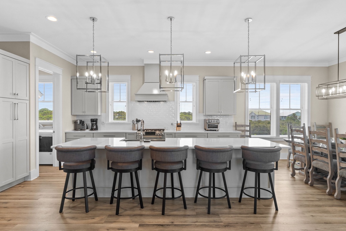 Spacious kitchen island with elegant pendant lighting and generous seating, flooded with natural light. Modern appliances perfect for culinary adventures and evening gatherings.