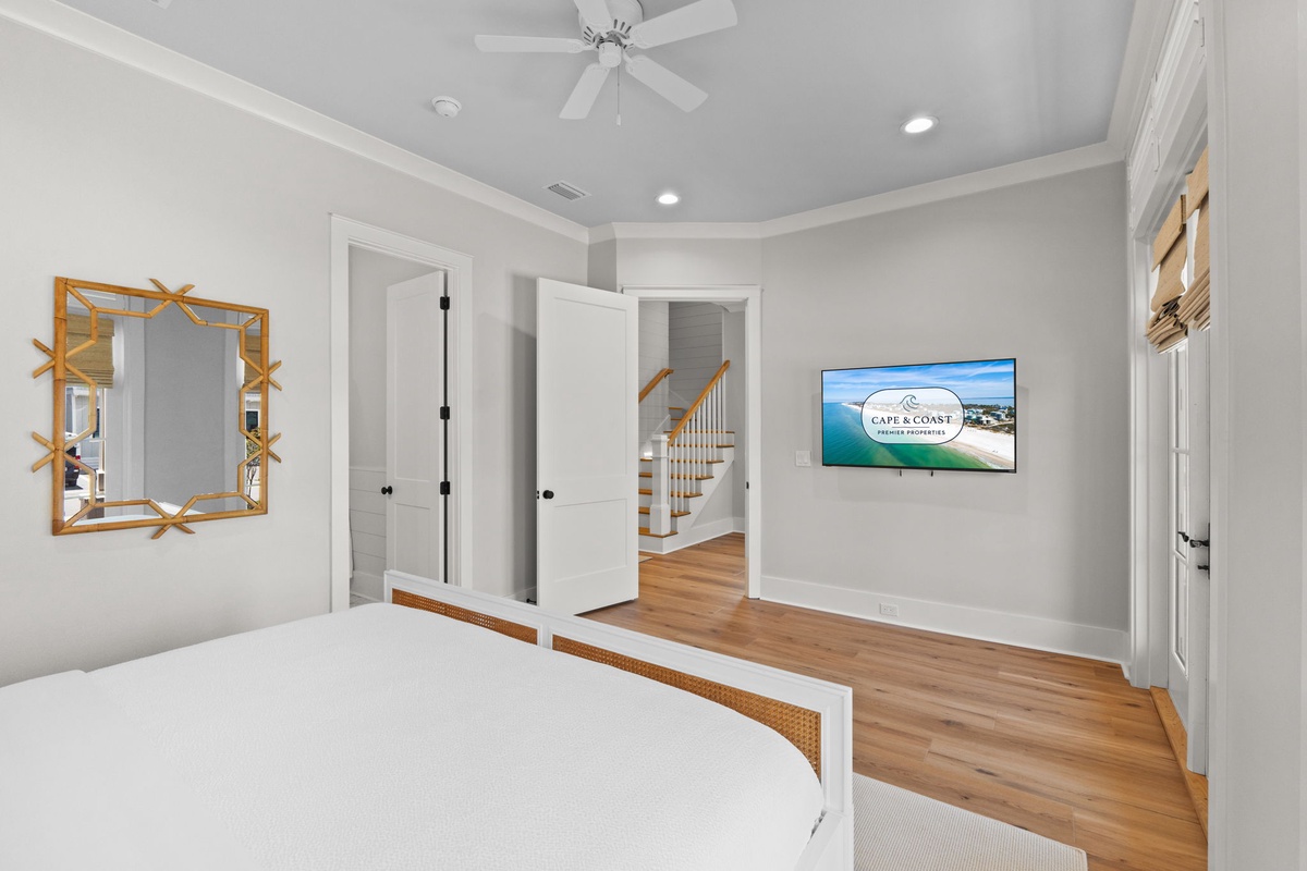 Relax in your private retreat with crisp coastal decor, a mounted TV for movie nights, and warm wood floors under a soothing ceiling fan.