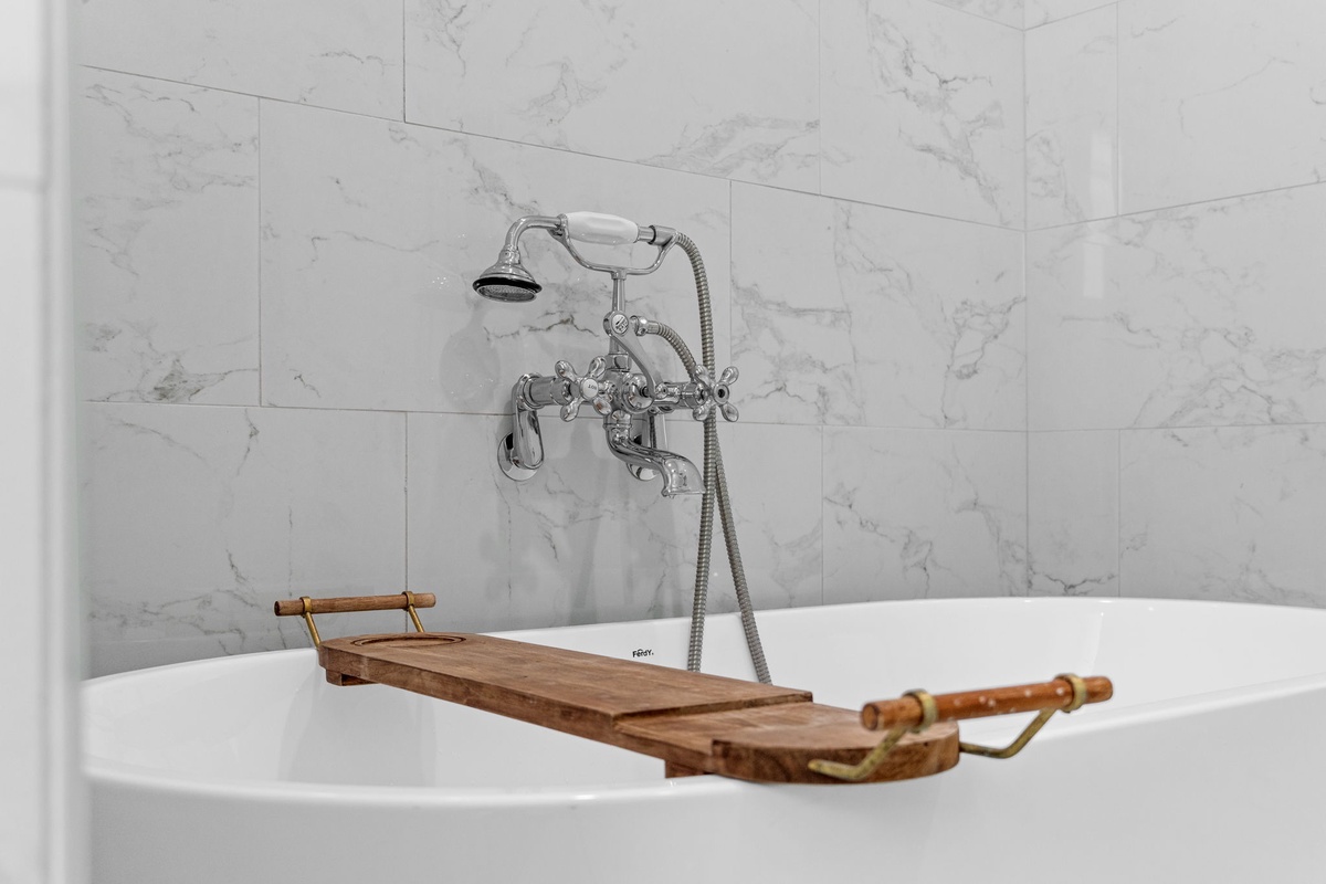 Sink into pure luxury with your elegant marble bathroom featuring a vintage-style tub and wooden caddy for ultimate relaxation.