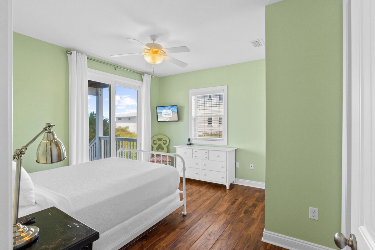 Unwind in this peaceful guest bedroom, where soft green walls and warm wood floors create a soothing sanctuary. Natural light streams in through the glass doors, inviting you to rest and recharge during your stay.