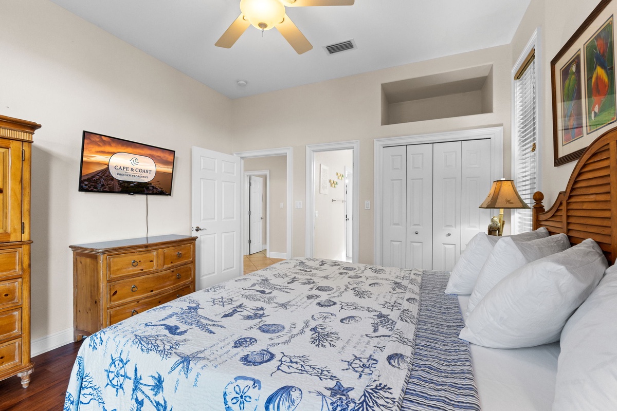 Relax in your peaceful bedroom with coastal-themed linens, flat-screen TV, and warm wood furnishings creating the perfect retreat.