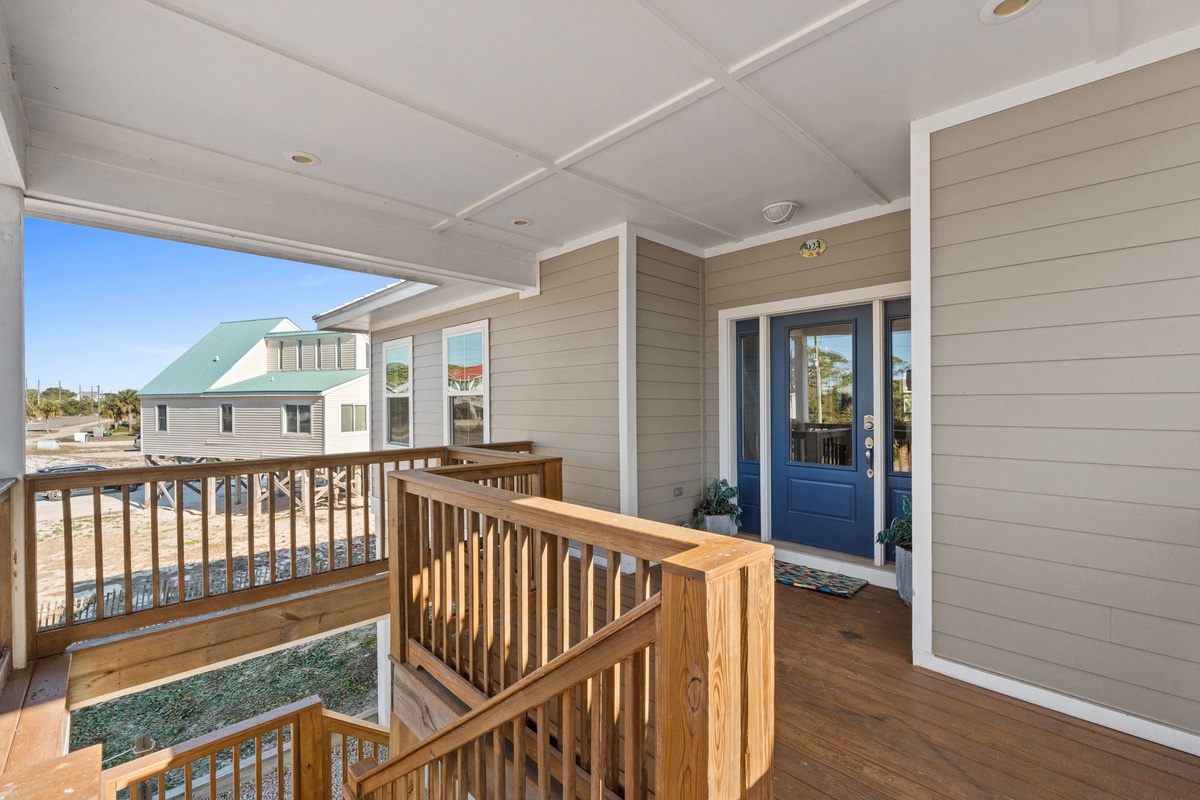 Coastal property entrance featuring elevated deck with wooden railings and blue front door, surrounded by neighboring beach homes.